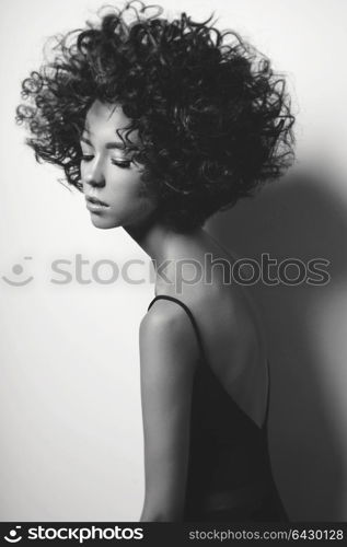 Black and white fashion studio portrait of beautiful woman in black dress with afro curls hairstyle. Fashion and beauty