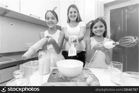 Black and white funny portrait of mother with two daughters posing on kitchen