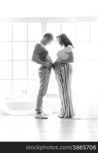 Black and white funny shot of pregnant wife and husband standing and touching by stomachs