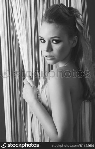 black and white , glamour indoor portrait of stunning blonde female with freckles on face, blonde hair and stylish make-up. She is covering her naked breast and looking in camera