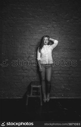 Black and white glamour photo of sexy woman posing against brick wall
