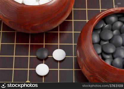 black and white go game stones and wooden bowls on goban