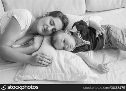 Black and white high point view photo of young mother sleeping next her baby boy lying in bed. Black and white photo of young mother sleeping next her baby boy lying in bed