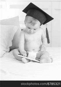 Black and white image baby in graduation hat using digital tablet