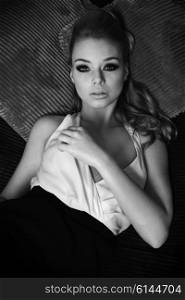 black and white image , fashion portrait of elegant pretty lady , she has noce hair style , and she is looking in camera with her stunning eyes , laying on pillow