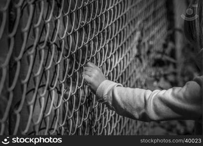 Black and white image of a little girl hand grabbing a metal fence, depicting drama