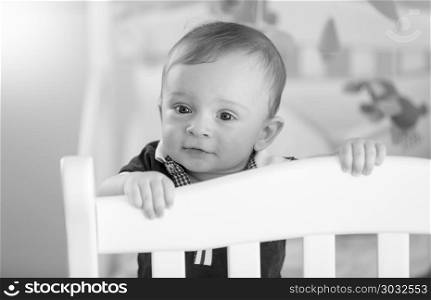 Black and white image of adorable baby boy standing in cot. Black and white photo of adorable baby boy standing in cot