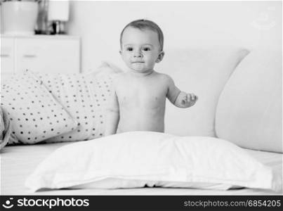 Black and white image of cute baby boy sitting on bed at bedroom