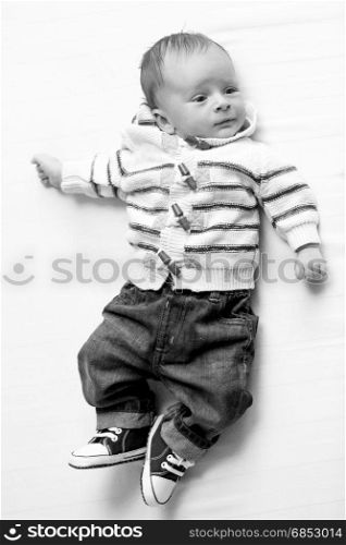 Black and white image of cute smiling baby boy in jeans and sweater lying on bed