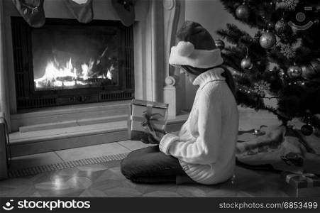 Black and white image of girl holding gift box and sitting next fireplace