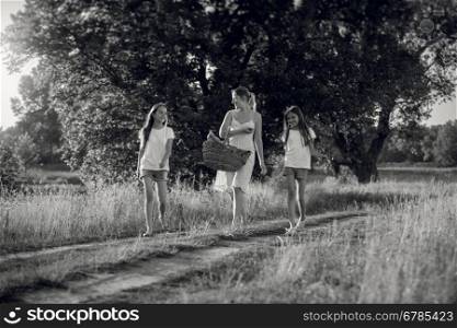 Black and white image of happy mother with daughters walking at meadow