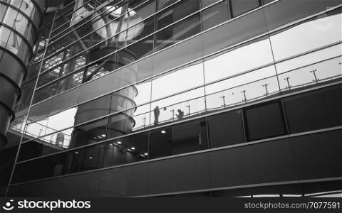Black and white image of people reflecting in modern glass building