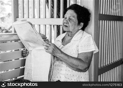 Black and white image of Senior asian woman Relaxing With Newspaper At Home