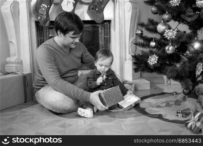 Black and white image of young father playing with his 1 year old baby boy next to Christmas tree
