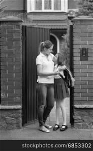 Black and white image of young mother standing with her daughter in school uniform at house backyard