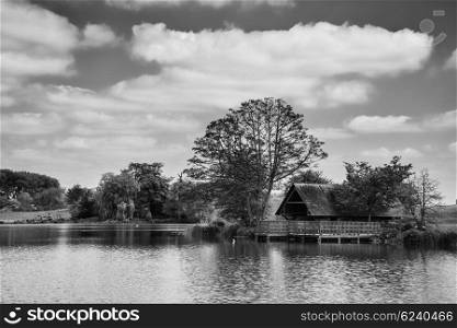 Black and white landscape image of boathouse on lake in Summer