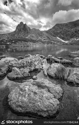Black and white landscape on the mountain lake with rocks at the front. Vertical view