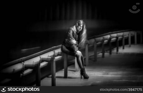 Black and white night shot of lonely woman sitting on railings at highway
