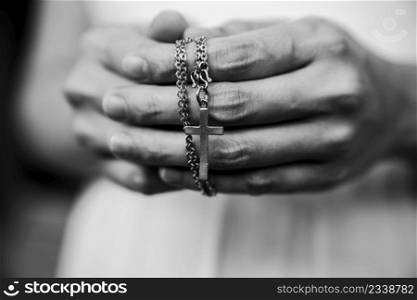 Black and white of woman hands praying holding a beads rosary with Jesus Christ in the cross or Crucifix on black background.