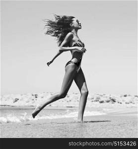 Black and white outdoor fashion photo of beautiful happy slender woman running on sea. Beach travel. Summer vibes