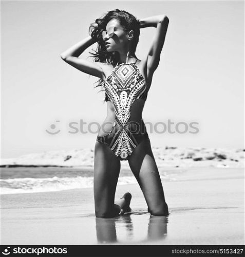Black and white outdoor fashion photo of beautiful happy slender woman sitting at sea. Beach travel. Summer vibes