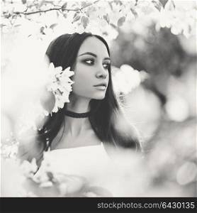 Black and white outdoor fashion photo of beautiful young woman surrounded by flowers of apple-tree. Spring blossom. Summer vibes