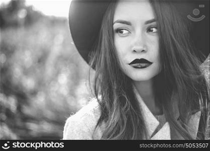 Black and white Outdoor fashion photo of young beautiful lady in autumn landscape with dry flowers. Gray coat, black hat, wine lipstick. Warm Autumn. Warm Spring