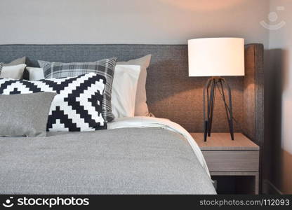 Black and white pattern pillows with gray blanket and white shade bedside table lamp