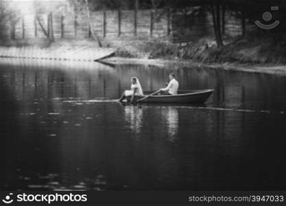 Black and white photo bride and groom riding on old wooden boat on lake