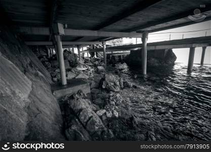 Black and white photo of beach under the old wooden pier