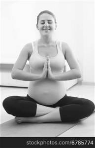 Black and white photo of beautiful pregnant woman practicing yoga at home