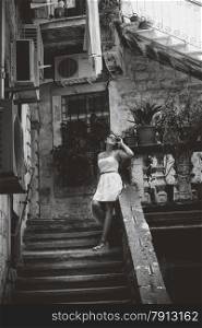 Black and white photo of beautiful woman in summer dress standing on old stone staircase