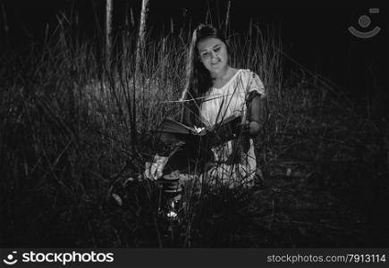 Black and white photo of beautiful woman reading book at night