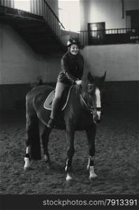 Black and white photo of beautiful woman riding horse in manege