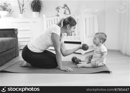 Black and white photo of beautiful young mother exercising on fitness mat with her baby boy