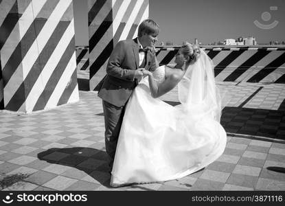 Black and white photo of bride and groom dancing on roof top at sunny day