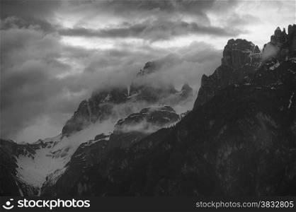 Black and white photo of cloudy sunset over Dolomites mountains. Italian Dolomites
