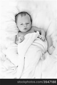 Black and white photo of cute baby boy covered in blanket on bed