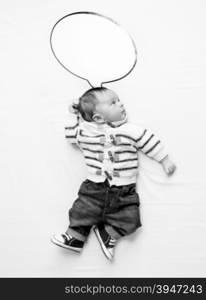 Black and white photo of cute baby boy with speech bubble lying on bed