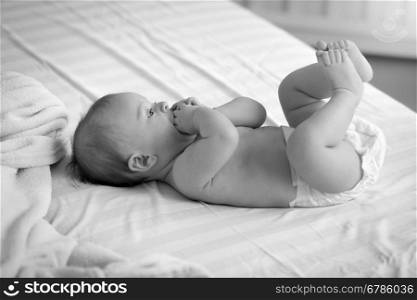 Black and white photo of cute baby in diapers lying on bed