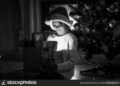 Black and white photo of cute smiling girl looking inside of glowing gift box at Christmas eve