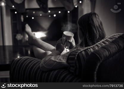 Black and white photo of cute woman sitting at fireplace with cup of tea