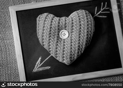 Black and white photo of drawn by chalk arrow going through knitted heart