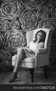 Black and white photo of elegant curly woman sitting in armchair