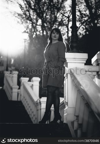 Black and white photo of elegant woman posing on stairs at park at sunny day