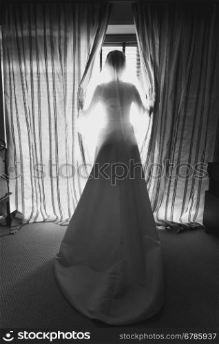 Black and white photo of elegant young bride in front of big window at hotel room