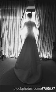 Black and white photo of elegant young bride in front of big window at hotel room