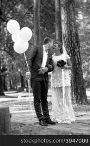 Black and white photo of groom holding balloons kissing beautiful bride at park