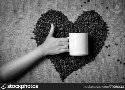 Black and white photo of hand with thumb up holding mug against heart made of coffee beans