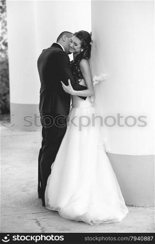 Black and white photo of happy just married couple kissing against row of big columns